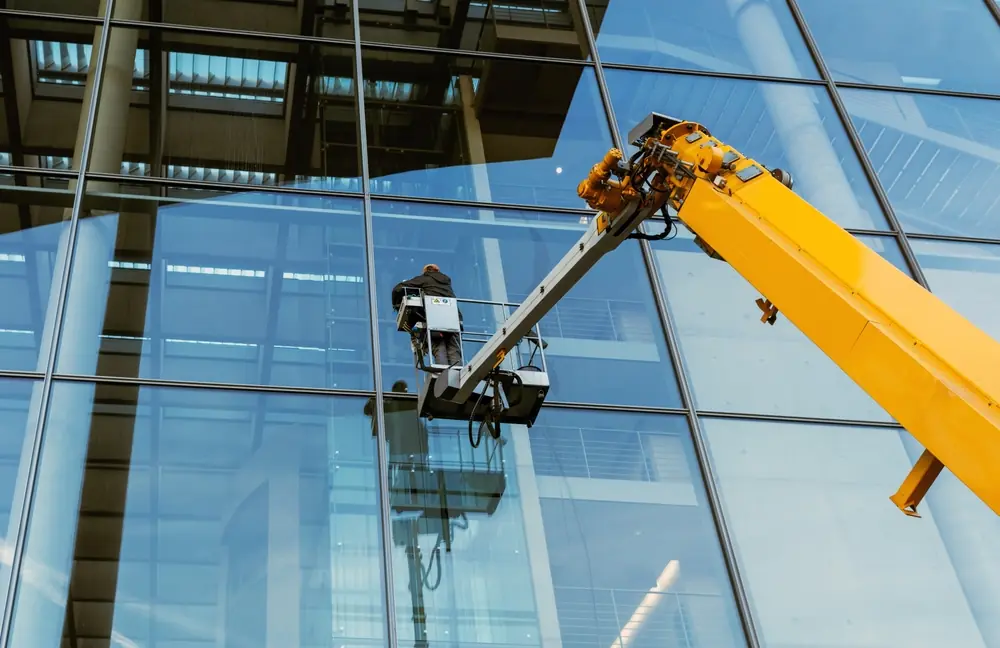 A yellow telescopic boom lift extended high against a modern glass skyscraper, demonstrating high-reach access for cherry picker hire. A yellow telescopic boom lift extended high against a modern glass skyscraper, demonstrating high-reach access for cherry picker hire.
